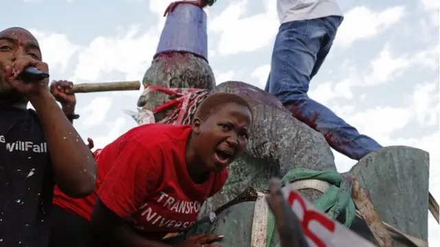 Students shout out as they climb on top of the decades old bronze statue of British colonialist Cecil John Rhodes, as the statue is removed from the campus at the Cape Town University, Cape Town, South Africa, Thursday, 9 April 2015