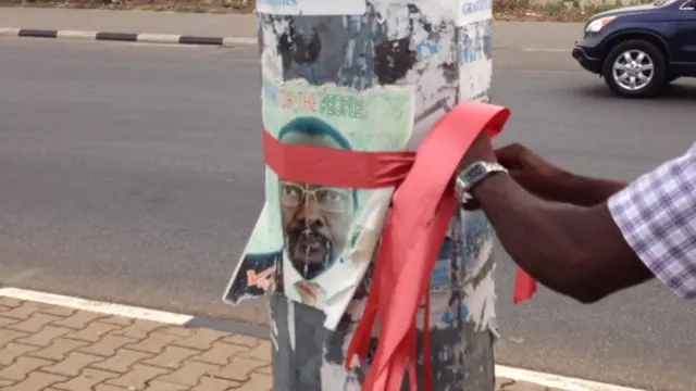 a campaigner ties a red ribbon to a lamp post in Abuja as part of a walk to remember the schoolgirls kidnapped by Boko Haram