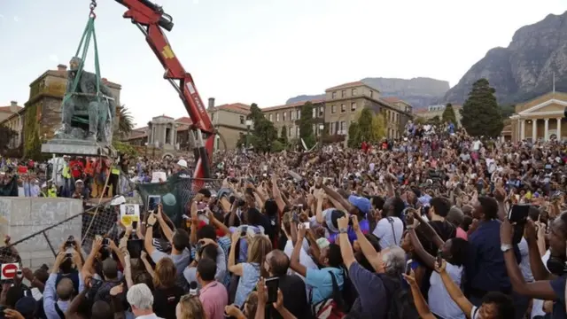 Students surround the decades old bronze statue of British colonialist Cecil John Rhodes, top left, as the statue is removed from the campus at the Cape Town University, Cape Town, South Africa,