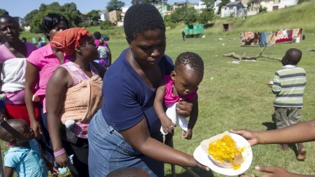 Women with children, who are the first to receive food, stand on a sports field in Chatsworth in the south of Durban