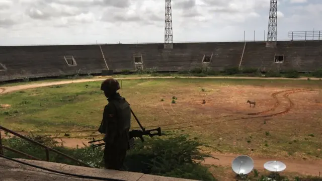 In 2011 A Ugandan soldier walks through the Banadir soccer stadium while an animal grazes