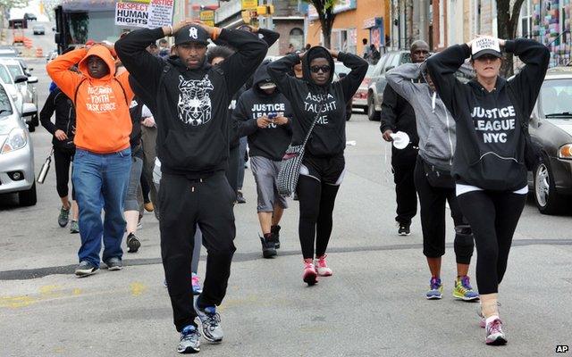 People walking down the street with their hands on their heads, as if they are being arrested