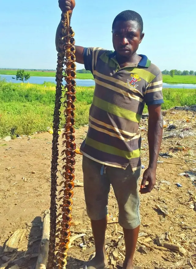 Philip Paul holding a skewer of frogs