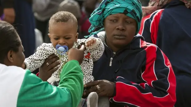 A migrant woman and a young child wait to board a ship in Lampedusa bound for Sicily