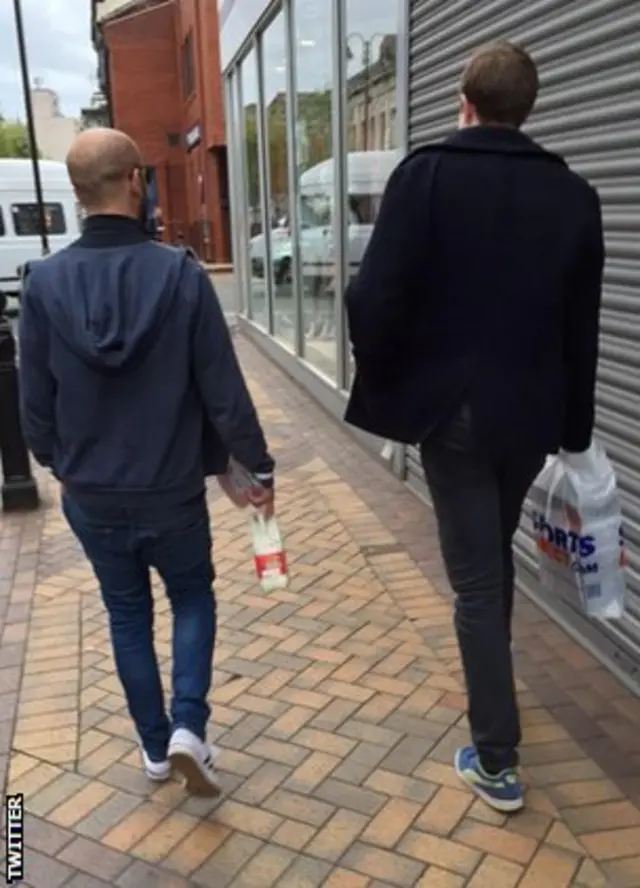 two men walking down a city street with their shopping