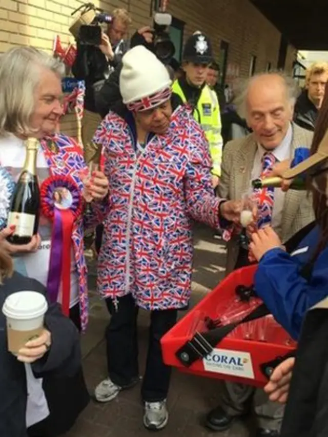 Royal watchers outside the Lindo Wing are given a drink of Prosecco