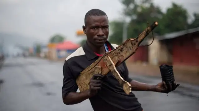 A man poses with a wooden rifle in the Musaga neighbourhood in Bujumbura, Burundi on May 5, 2015.