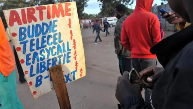 Avendor, holding US dollar notes, sells phone cards outside a market in Harare, Zimbabwe - April 2010