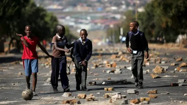 Boys joke as they walk from school on a street filled with stones left behind by protesters who were dispersed by police in Soweto, South Africa - 7 May 2015