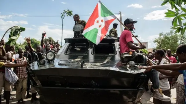 A man holding a Burundi's flag stands on a tank as people take to the streets to celebrate, waving branches, beeping car horns and parading through Bujumbura on 13 May 015