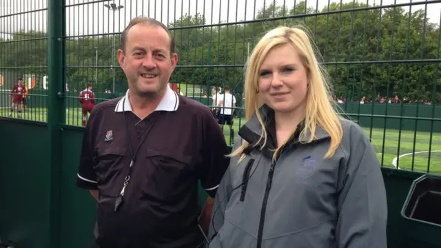 A referee and a pitch manager stand side by side to camera with a pitch in the background