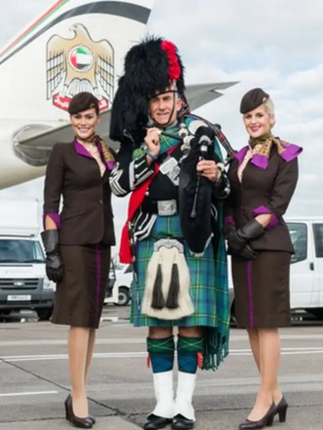 A man in piper's uniform flanked by two Etihad stewardesses