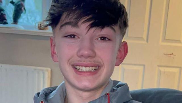 Christopher McBurnie, a teenager with short dark hair and a long fringe, smiling.