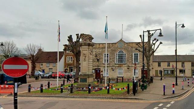 War memorial set in a grass square with flags in front of the town hall