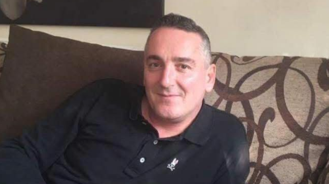 A man smiles at the camera while sitting in a living room.
