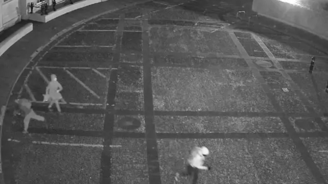 Grey CCTV footager of three people running across the car park at County Hall