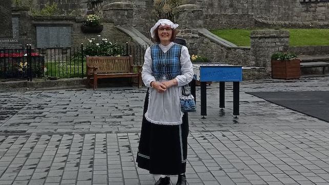 Diane Tyrer, a woman wearing traditional Manx dress smiles, you can see the table football in the background.