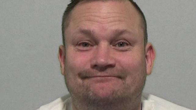 Mugshot of Matthews. He has a smirk on his face and has very short cropped dark hair and a stubbly beard.