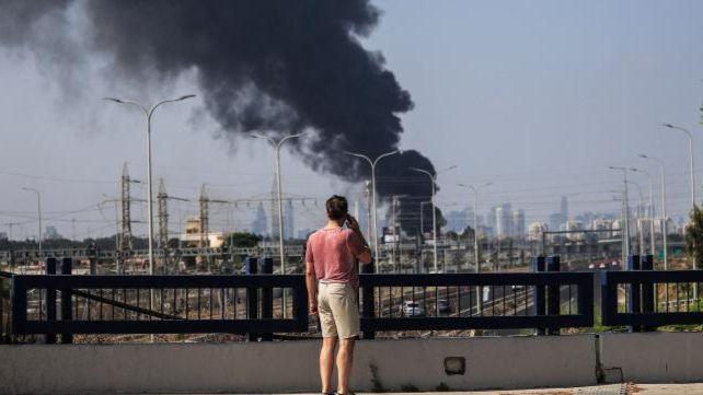 An Israeli man looks at smoke that rises following a missile attack from Iran, in Herzliya, Israel,