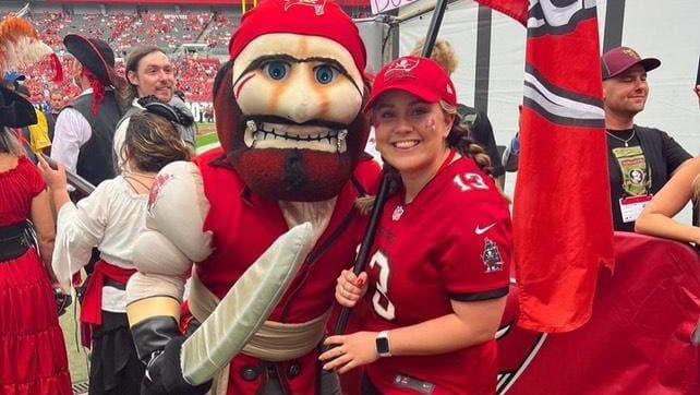 Christie Thomas in a red shirt holding up a flag next to a mascot.