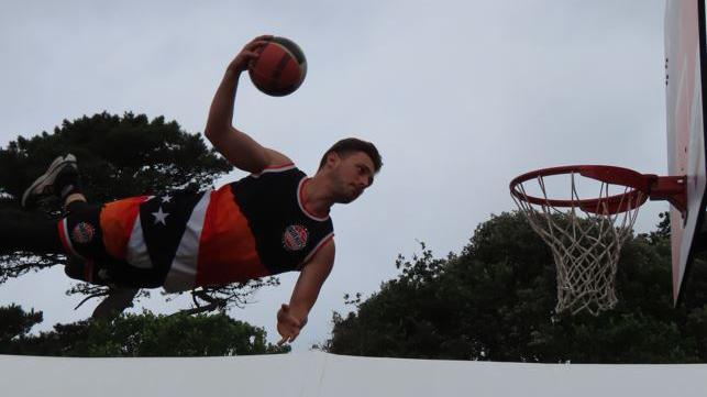 A basketball player prepares to slam dunk the ball into a hoop during an acrobatic display at the North Show in Guernsey.