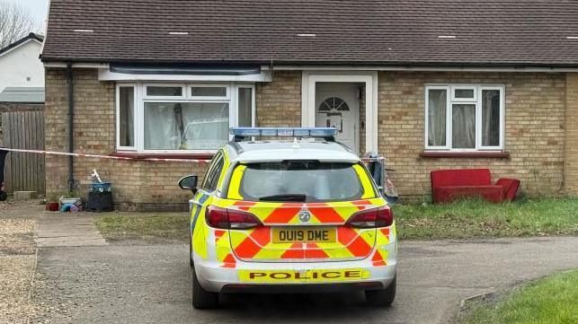 A police vehicle outside a bungalow in Grounds Avenue, March. The house has two windows, a door and tape across the front of the house. 