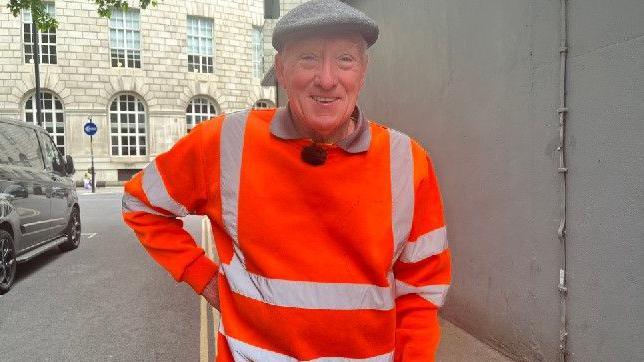Archie Workman in a flat cap and hi-viz overalls near Manchester Central Library