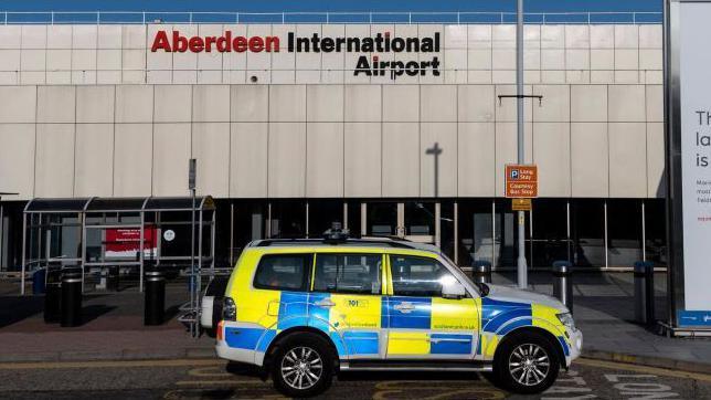 Blue and yellow checked police vehicle outside Aberdeen Airport building