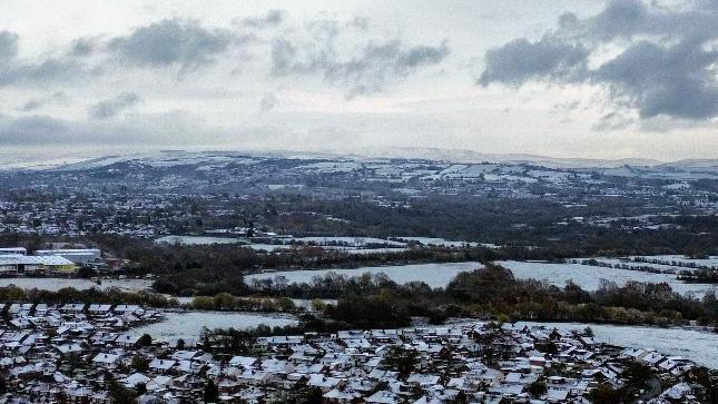 Snow-covered panorama with houses and trees in the foreground and hills in the background