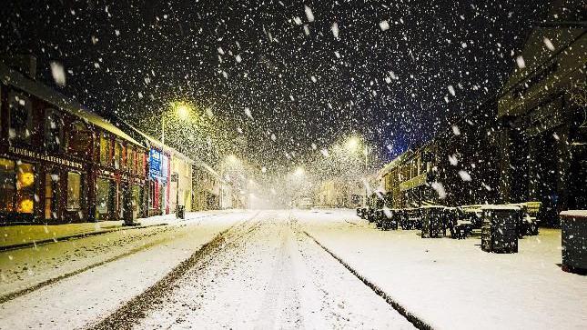 A snowy street scene taken in Carrickmore, County Tyrone. Tyre tracks are visible on the road, fresh snow is falling