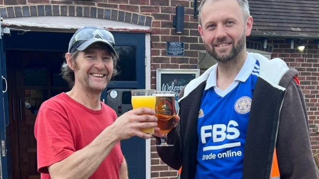 Bob Lee in a red t-shirt raising a glass with volunteer Sam Laywood