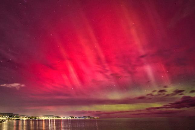 The lights from the coastline can be seen on the left with pink and green lights in the sky from the Northern Lights.