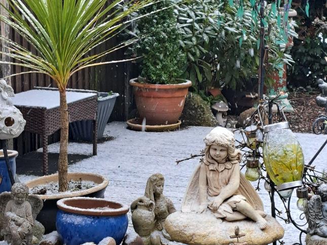 Snow falling on a garden with ornaments and potted trees