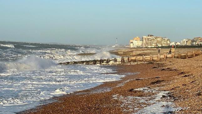 A beach on a sunny morning. High winds are causing large waves. 