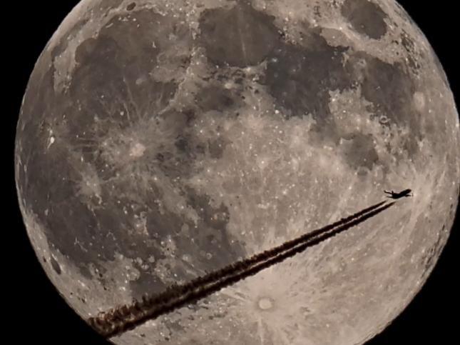 A black and white image showing streak marks from a plane as it crosses the supermoon.