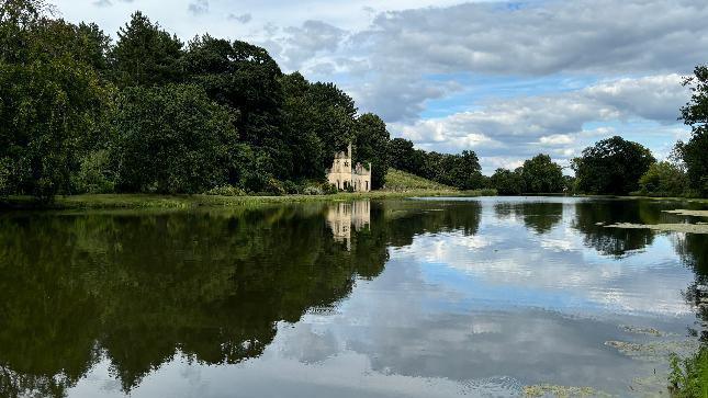 A river reflecting trees and a house, all under a blue sky