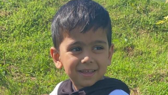 A young boy with short brown hair smiles as he looks away from the camera.