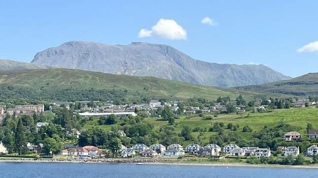 A large mountain with a single white cloud above it and some houses and green landscape in the foreground.