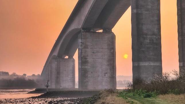 Concrete bridge crosses river illuminated by pink skies