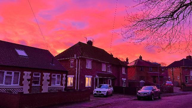 A row of homes in Cromer with cars outside. The sky is a vivid orange with sections of purple