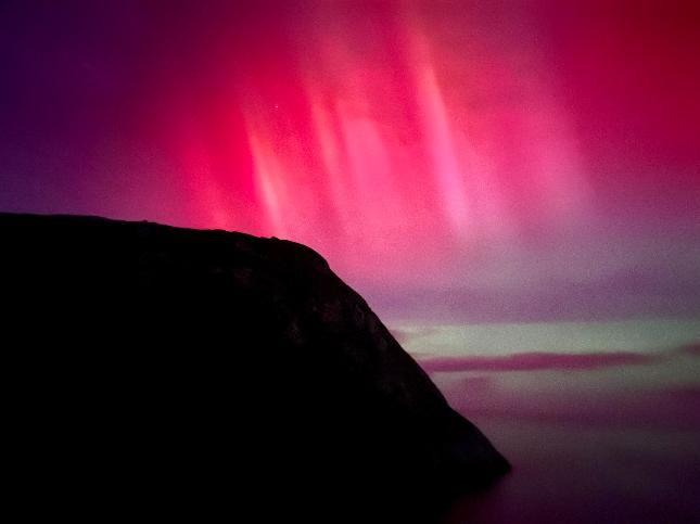 The silhouette of what looks like the roof of a building can be seen on the left with pink and green lights seen in the sky.