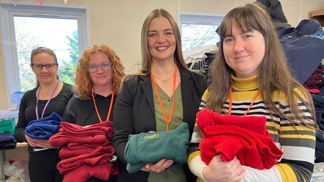 Four female volunteers at Uniform Exchange holding donated school clothes.