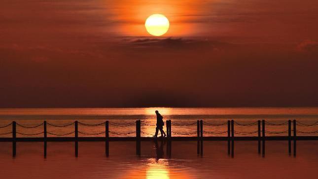 The moon is visible from a beach at sunset.