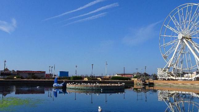 An image of the big wheel in Hastings, East Sussex. One bird can be seen on the lake. 