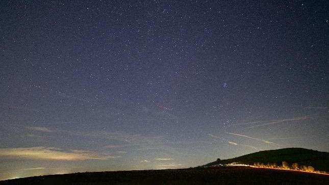 A night shot of a deep blue starry sky with the silhouette of a hill below.