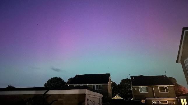 The Northern Lights with a green, purple and pink tinge, and buildings in the foreground.