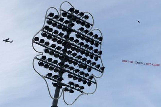 A plane flying over a cricket pitch with a banner saying "India stop genocide & free Kashmir"