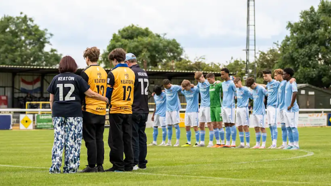 Family members and footballers stand on the pitch with their heads bowed