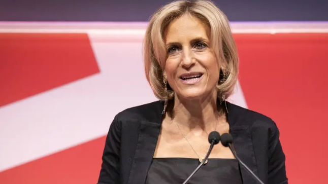 A blonde-haired woman in a dark jacket by a microphone