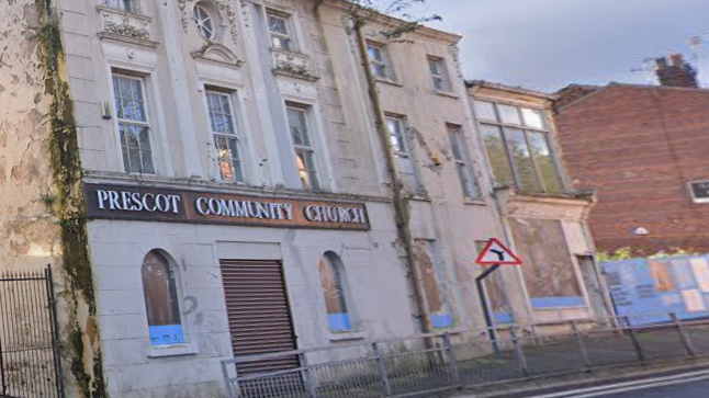 An earlier image showing the cinema building before restoration. It is boarded up, overgrown and bears a sign saying Prescot Community Church across the front 